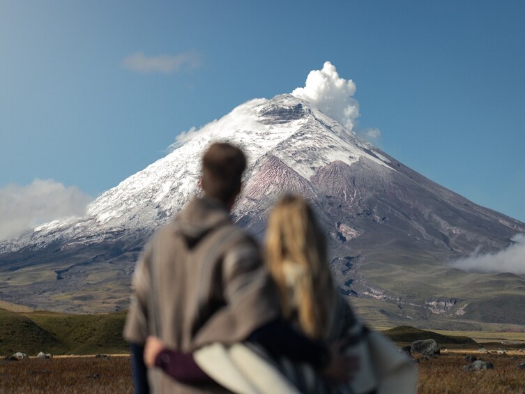 A couple embracing in a field with a snow-capped mountain in the background. 1