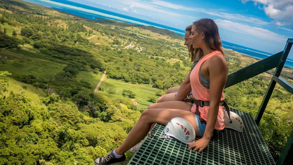 A person sitting on a metal platform overlooking a lush green landscape with a view of the ocean. 5