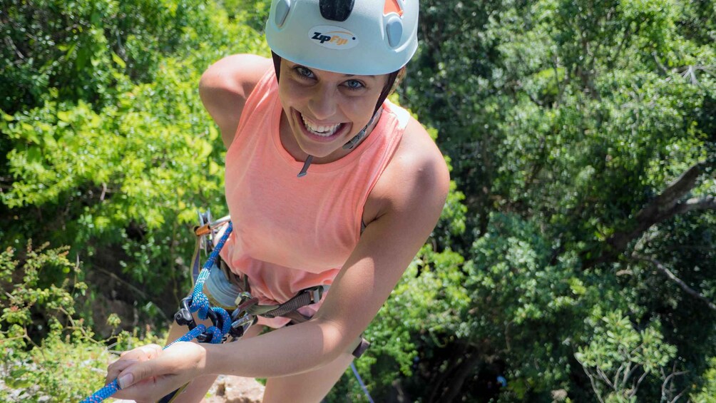 A person in a helmet and orange top climbing a tree. 2