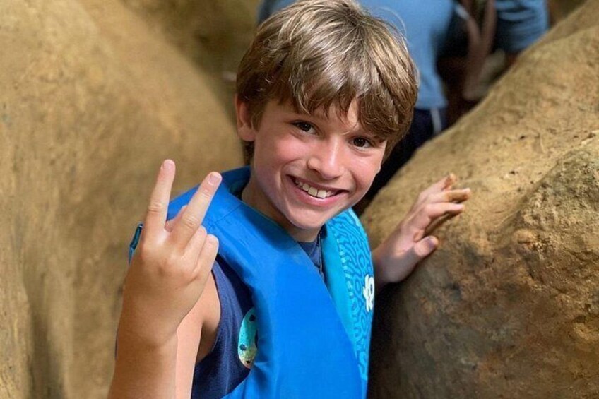 A child in a blue shirt with a peace sign, standing next to a large rock formation. 2
