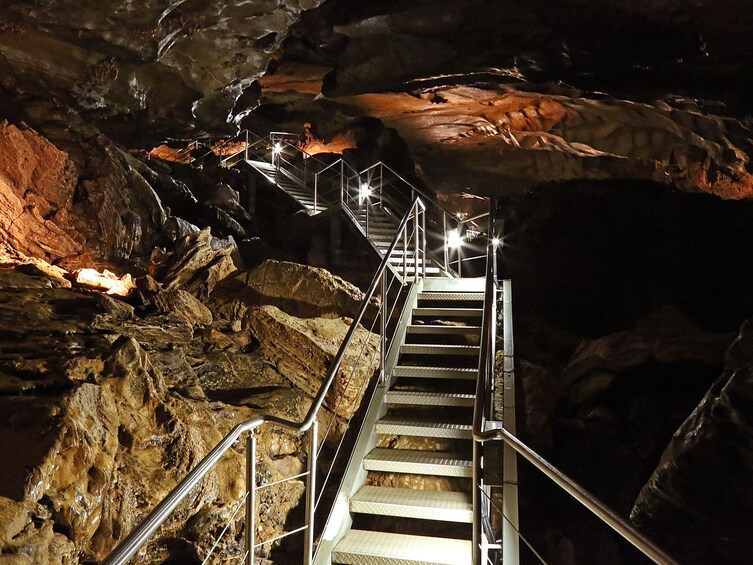 A metal staircase leading upwards in a cave with rocky walls and artificial lighting. 1