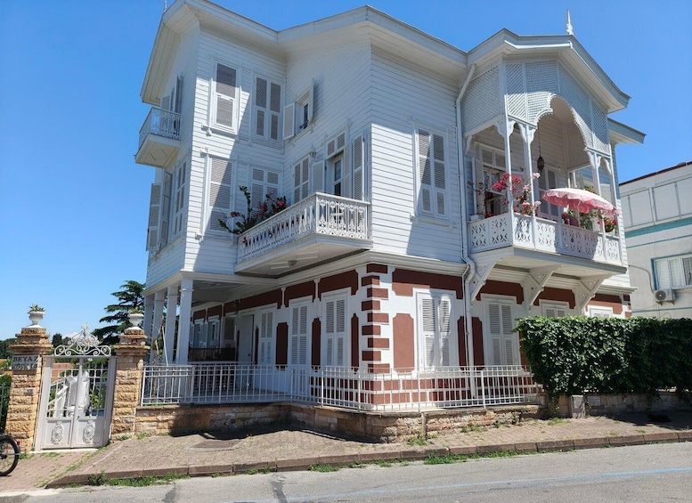 A multi-story white building with red accents, balconies with white railings, and a gated entrance. 4