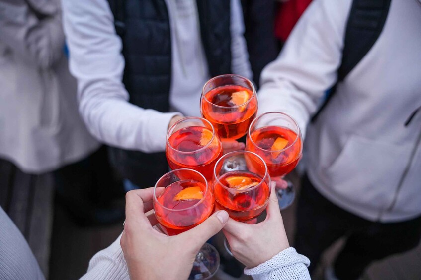 A group of people holding glasses with a red beverage, possibly a cocktail, with an orange slice garnish. 3
