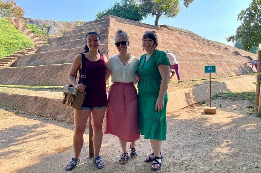 Three people standing in front of a large earthen structure with a sign indicating a historical site. 5