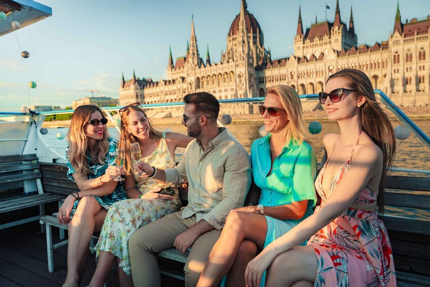 A group of people sitting on a bench by a river with a historic building in the background. 4