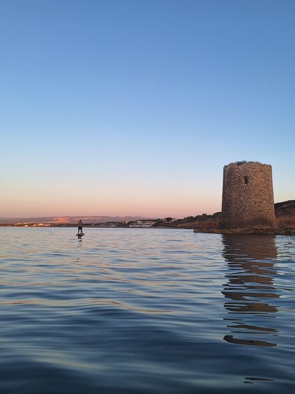A calm body of water with a stone tower in the foreground and a person standing in the water. 2