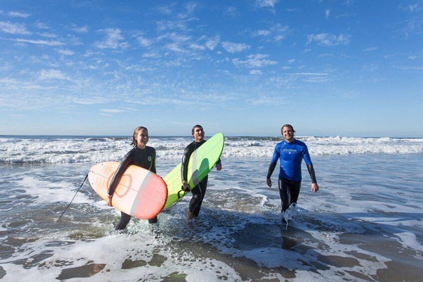 Three people walking on a beach with surfboards. 2
