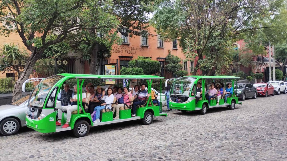 Two green trolley buses parked on a cobblestone street with passengers. 4