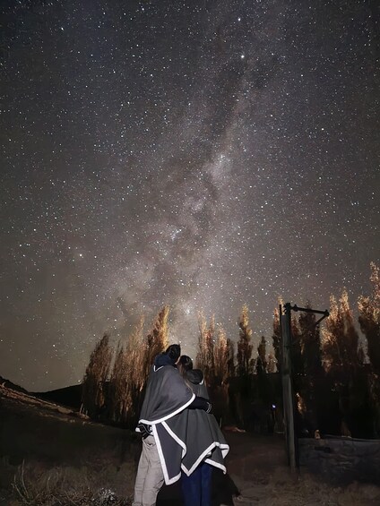 A night sky filled with stars, a person in a dark jacket, and a wooden structure. 4