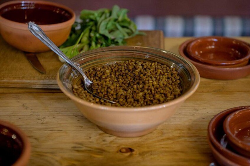 A bowl of lentils with a spoon, surrounded by clay bowls and a wooden cutting board. 5