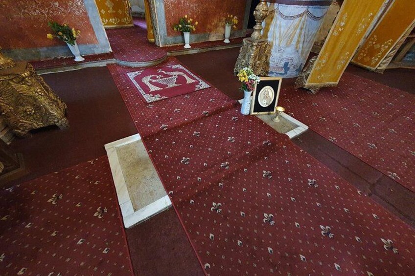 Interior de iglesia con suelos cubiertos de alfombra roja, un icono religioso enmarcado y un mantel blanco sobre el altar. 1