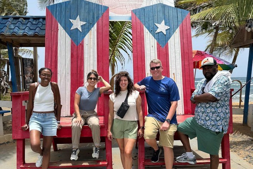 A group of people sitting on a bench with a Puerto Rican flag backdrop. 5