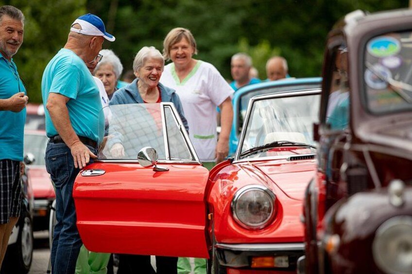 A red vintage car with its door open, surrounded by people. 3