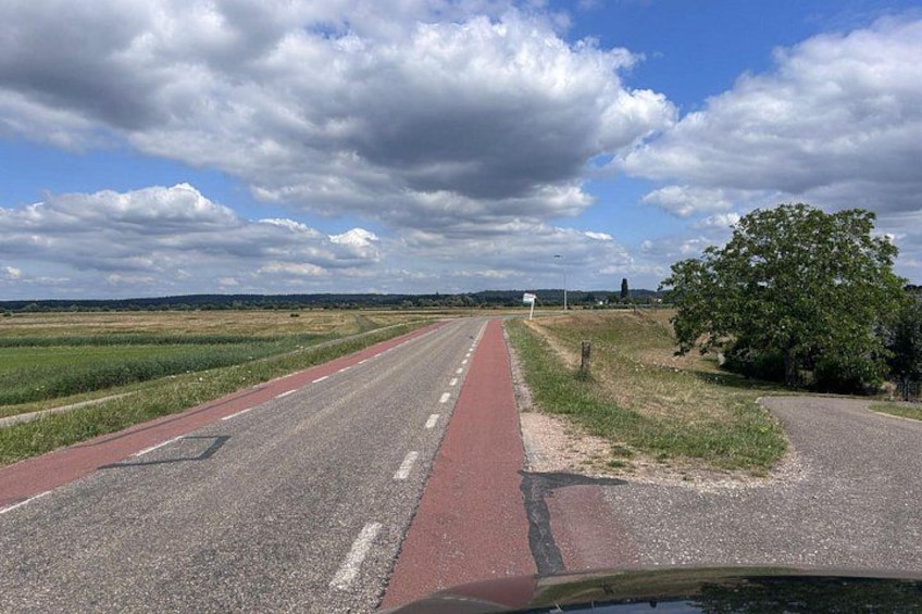A rural road with a red bike lane, surrounded by fields and a cloudy sky. 2