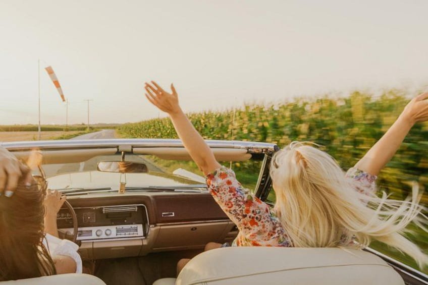 A convertible car driving on a road with a person raising their hand. 4