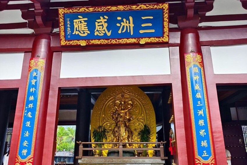 A temple entrance with a golden statue, red pillars, and Chinese characters. 4