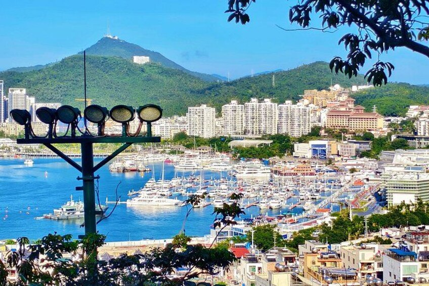 A coastal cityscape with a marina, buildings, and a hill in the background. 1