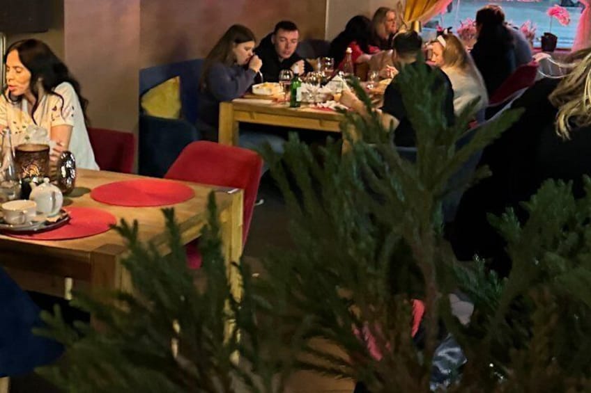 En restaurant med borde, stole, spisende gæster og juletræer i forgrunden. 2
