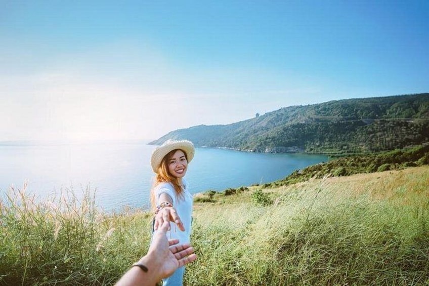 A person extending their hand towards another person in a grassy area with a lake and hills in the background. 4