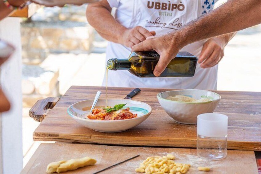 A person pouring olive oil into a bowl, with pasta and a knife on a wooden table. 2