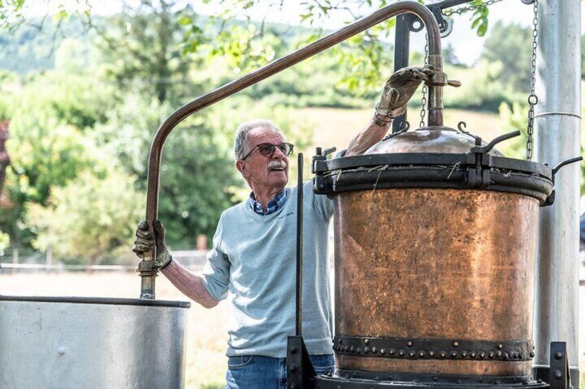 An elderly man operating a large copper still. 5
