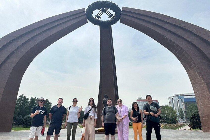A group of people standing in front of a large, arch-shaped monument with a circular top. 3