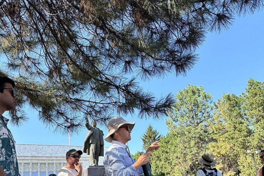 A group of people observing a statue under pine trees. 1