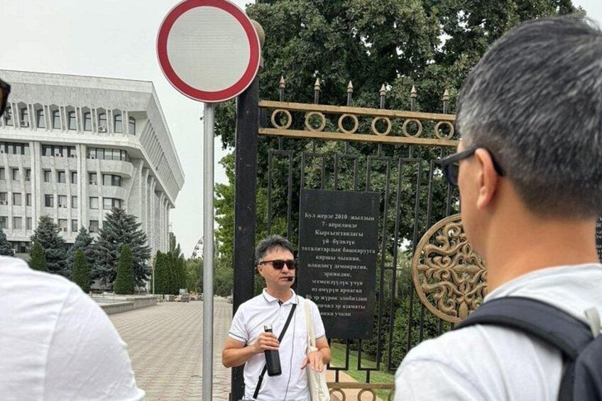 A man standing in front of a gate with a sign, a building in the background, and trees. 2