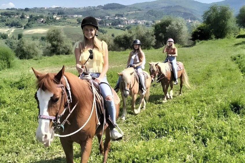 Three people riding horses on a grassy field with a mountainous landscape in the background. 5
