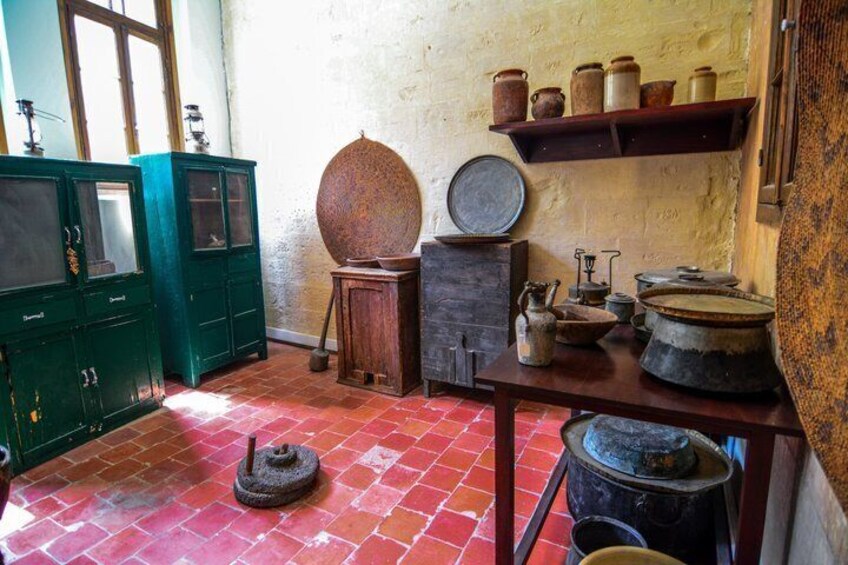 Een landelijke keuken met groene kastjes, een vloer van rode tegels en divers oud keukenmateriaal. 3