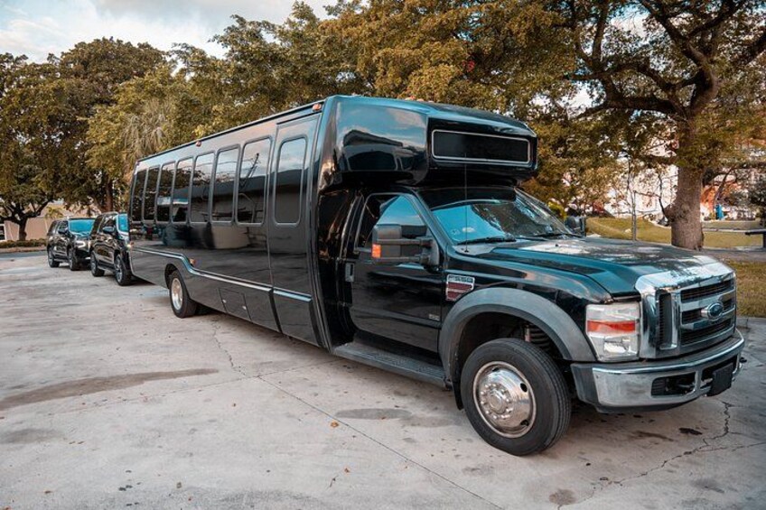 A black bus parked on a concrete surface with trees and a building in the background. 2