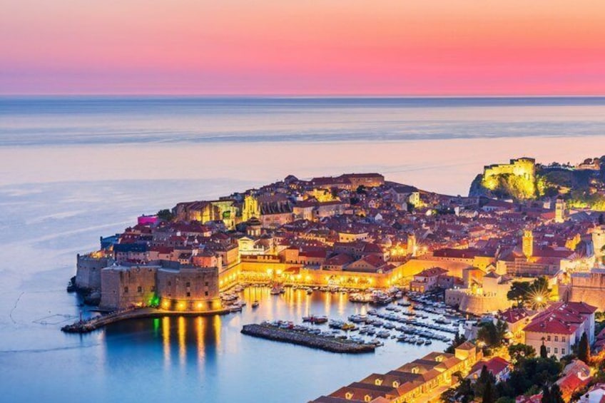 Un paysage urbain côtier au crépuscule, avec des bâtiments illuminés, un château imposant perché sur une colline et une mer calme. 3