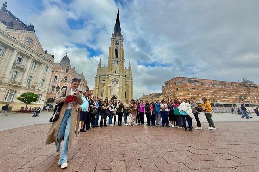 A group of people standing in a square with a historic building in the background. 1