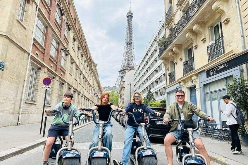 A group of people riding electric scooters on a street with the Eiffel Tower in the background. 2