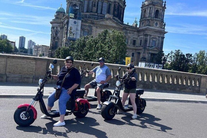 Three people on electric scooters in front of a historic building. 3