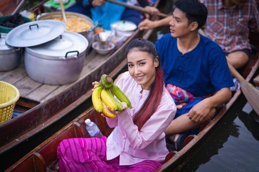 Een persoon in een boot, met bananen in de hand, terwijl er in de verte kookpotten en manden staan. 3