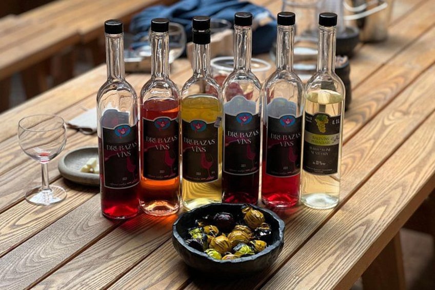 Una mesa de madera con seis botellas de vino Dr. Vass y un bol de aceitunas. 4