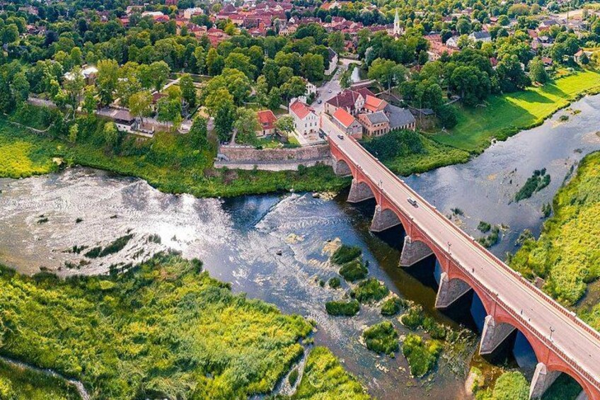 Un puente rojo sobre un río, rodeado de vegetación y edificios. 1