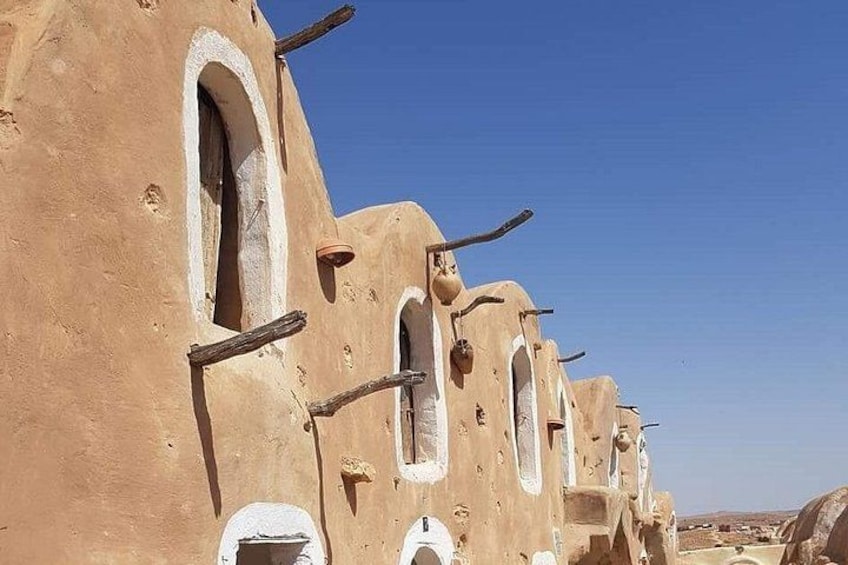 A row of traditional mud-brick buildings with arched windows and wooden beams. 3