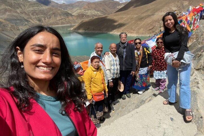 A group of people standing on a mountain ledge with a lake in the background. 5