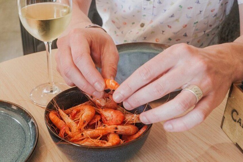 En person som lagar mat, och som just nu håller på att hantera räkor. På bordet står en skål med räkor och ett glas vitt vin. 4