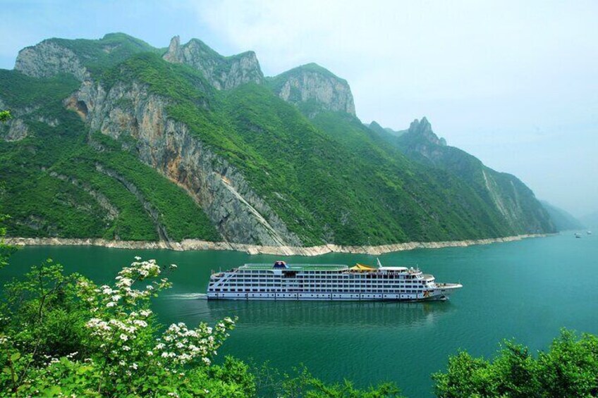 A cruise ship on a calm river with green cliffs in the background. 1