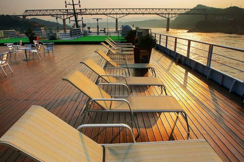 A wooden deck with lounge chairs and potted plants, overlooking a river with a bridge in the background. 4