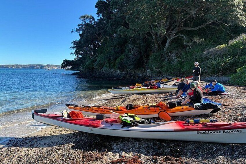 Kayaks on a pebbled beach with people sitting and standing, a clear sky, and a calm sea. 2