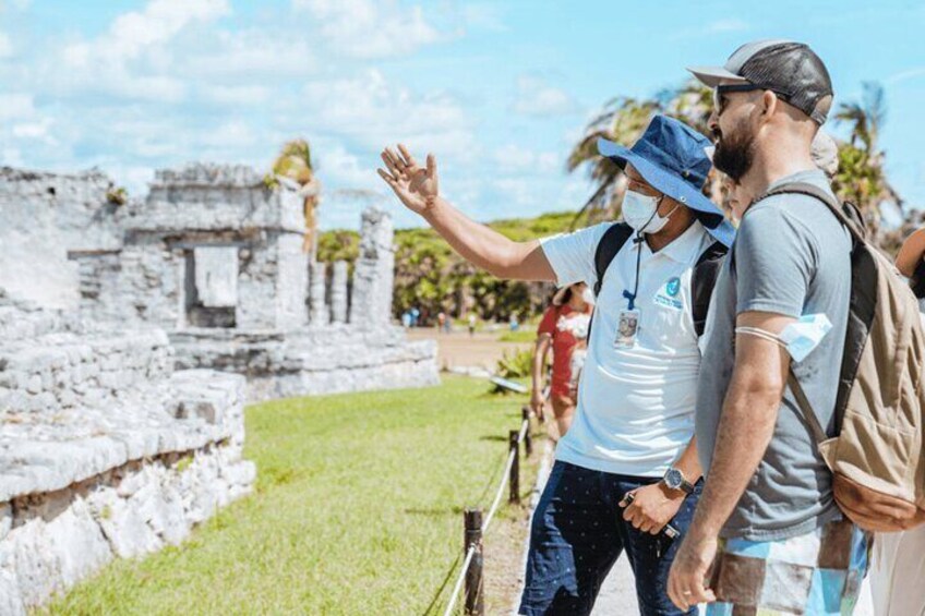 Two people standing near ancient ruins with a guide pointing out features. 3