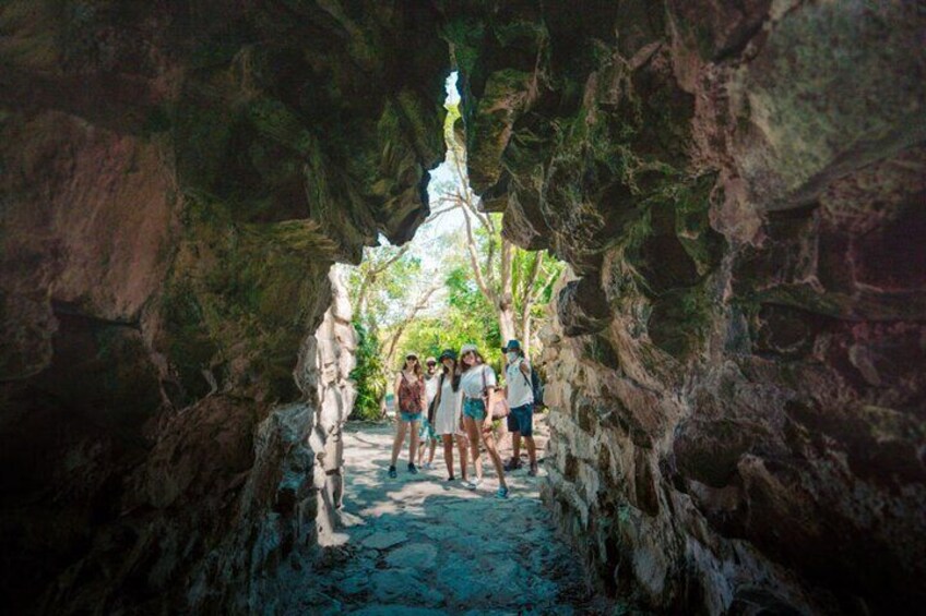A group of people walking through a narrow cave passage with rocky walls and a small waterfall. 4