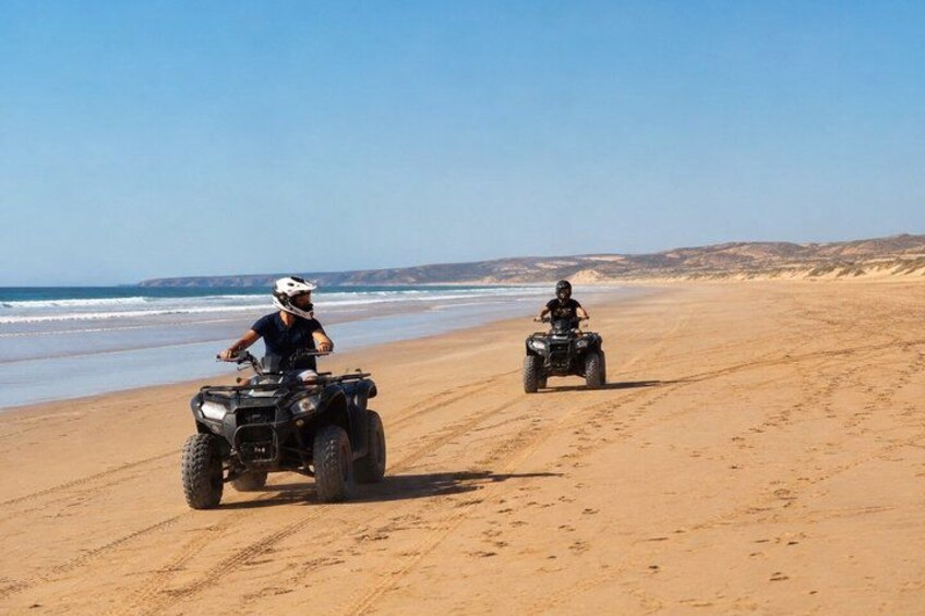 Two people riding ATVs on a sandy beach with the ocean in the background. 3