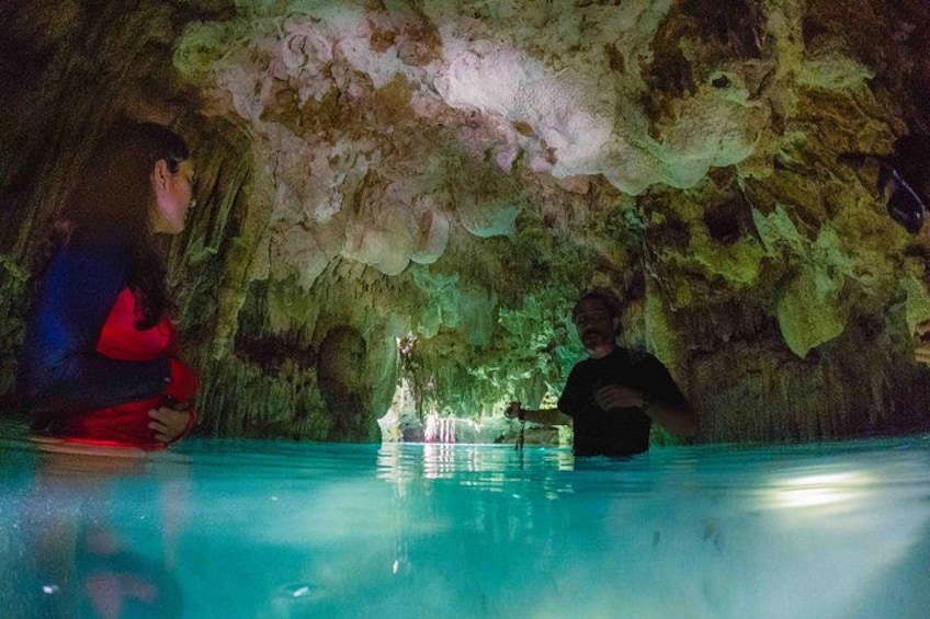 A cave with stalactites and stalagmites, a pool, and a person standing in the water. 2