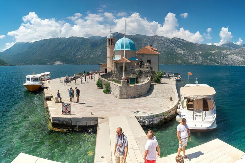 Un muelle con barcos, un pequeño edificio con cúpula azul y montañas al fondo. 3