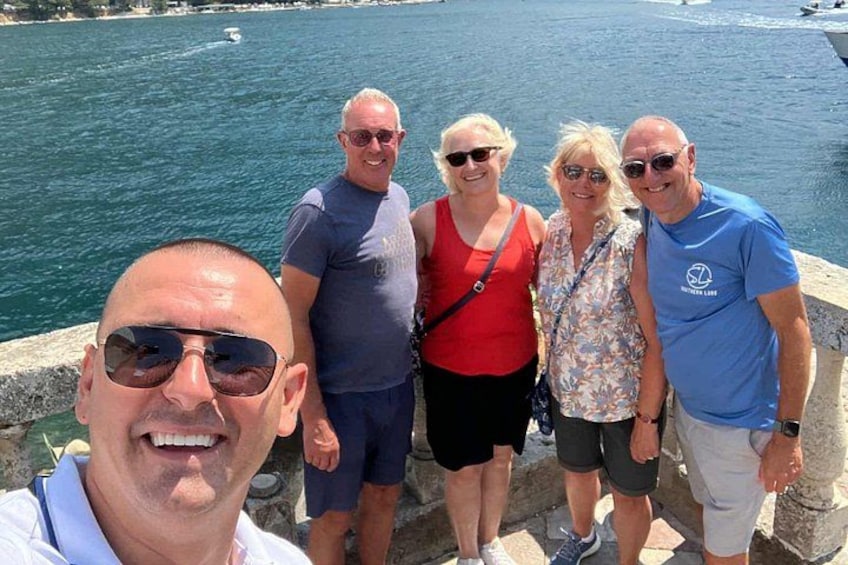 A group of people standing by a waterfront with a body of water and a distant boat in the background. 4
